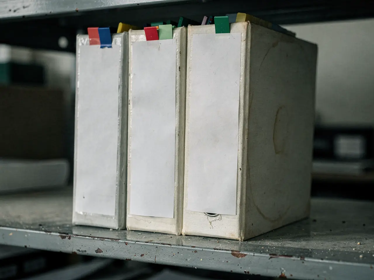 Worn ring binders of paper manuals with coloured index tabs on a metal shelf.